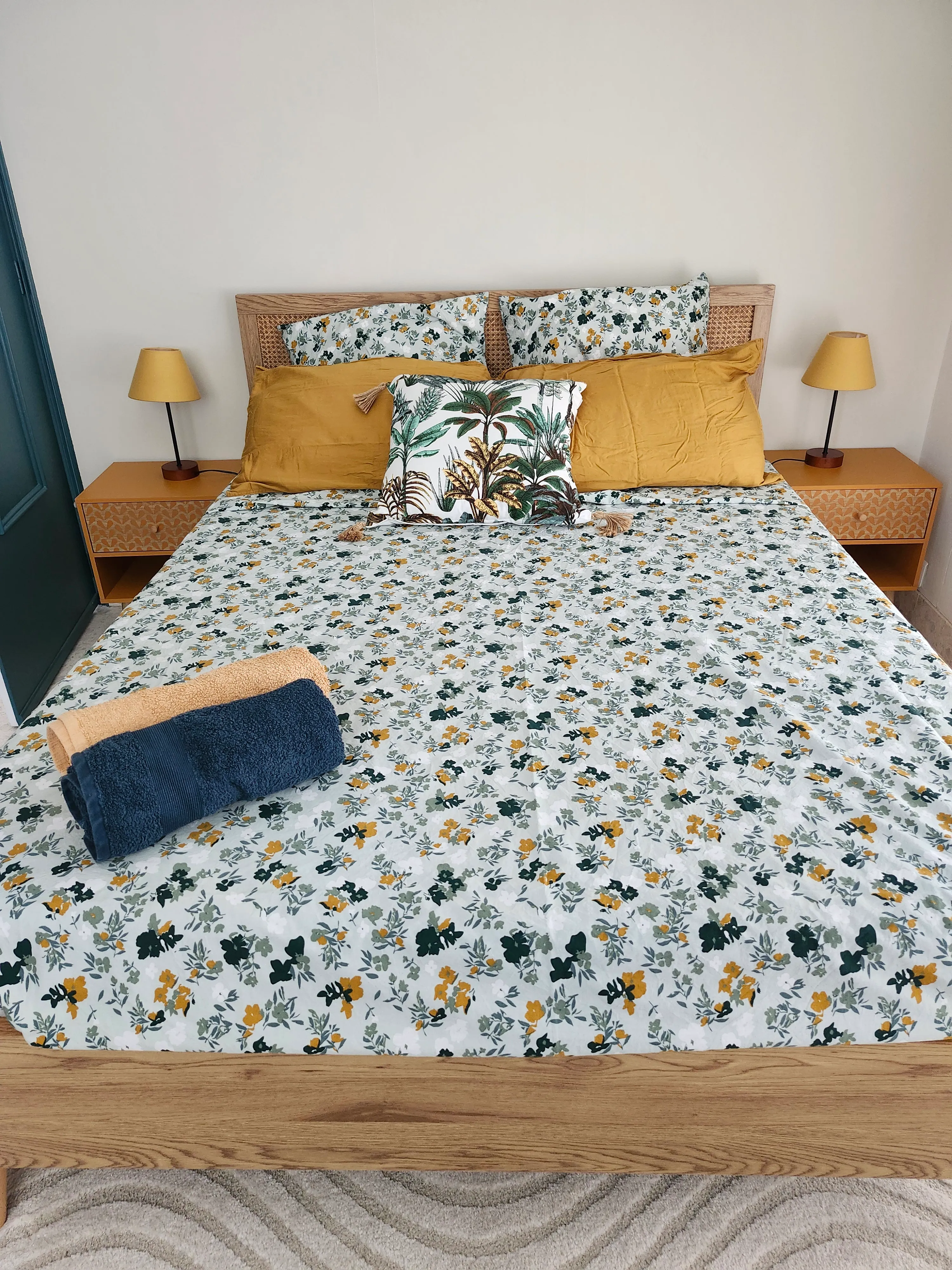 Chambre Céladon : lit double, parure fleurie et coussins moutarde