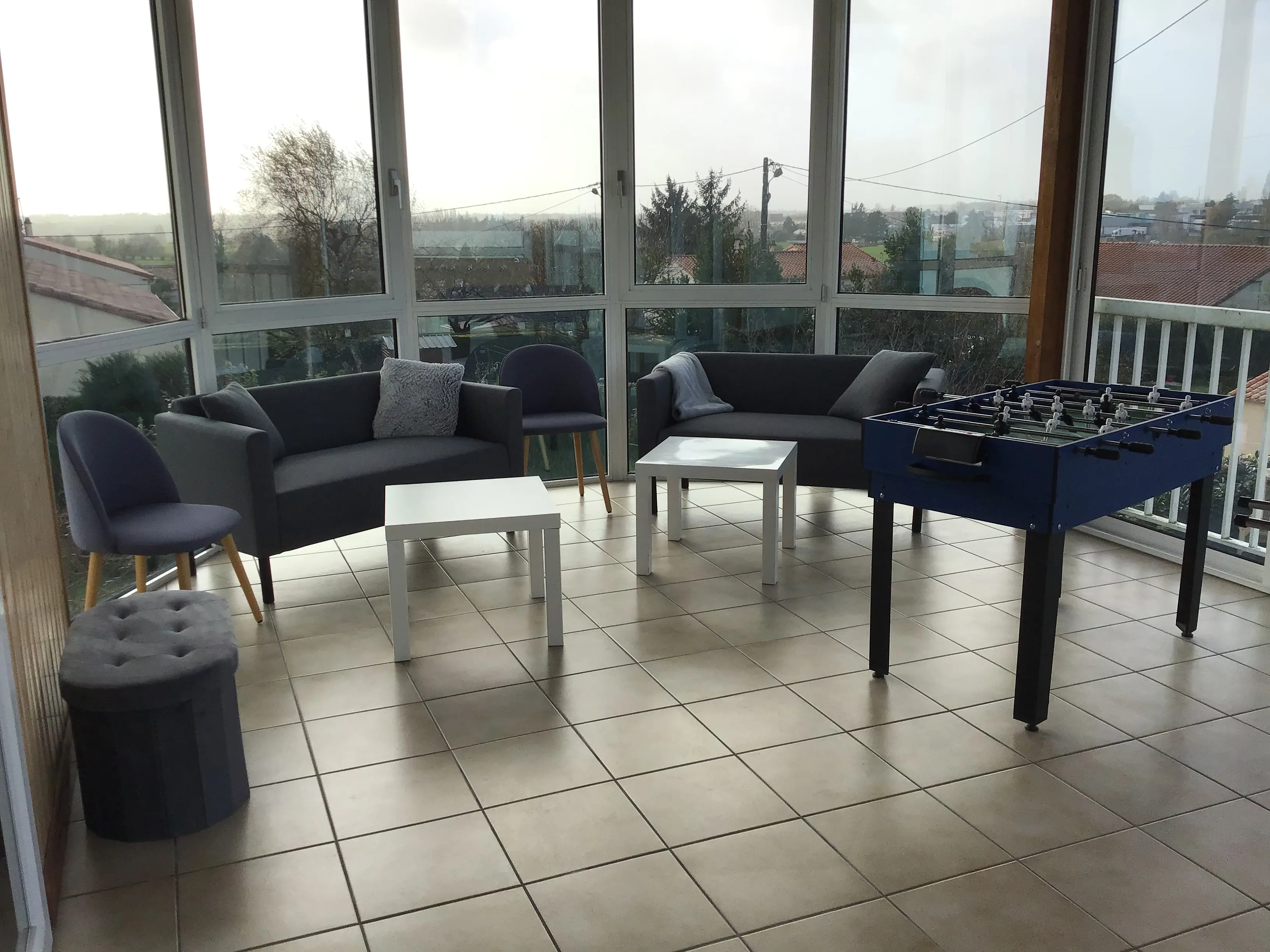 Véranda de l’étage du gîte de Mellonia : canapés, fauteuils et baby-foot avec vue sur le bocage